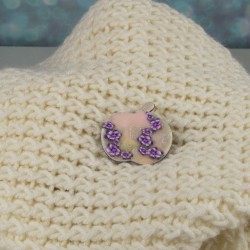 Broche posée sur un lainage, fond dans les transparences, fleurs lumineuses violettes
